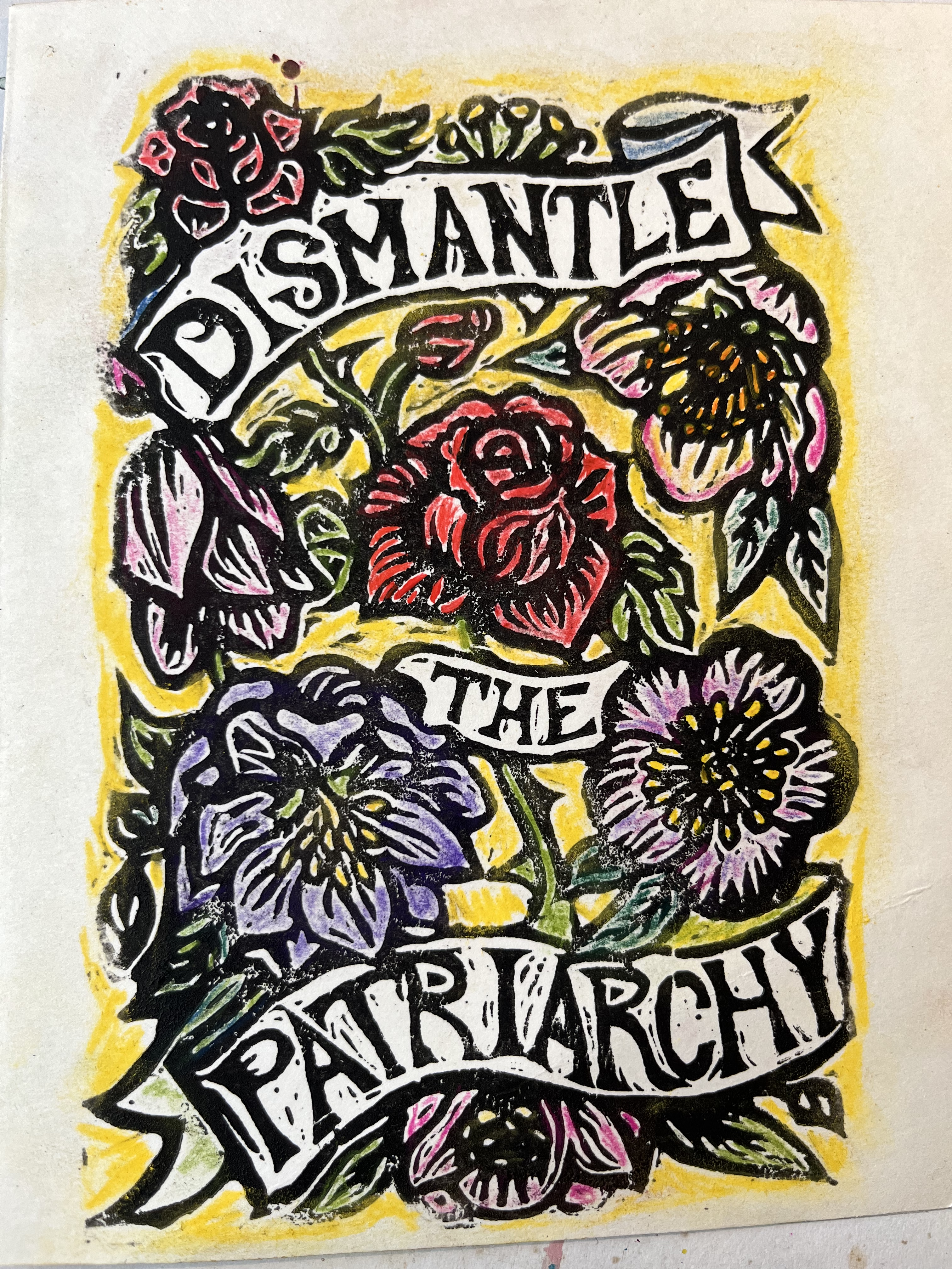 A linoleum block print colored with colored pencils with text "Dismantle the Patriarchy" on a ribbon surrounded by roses and hellebores
